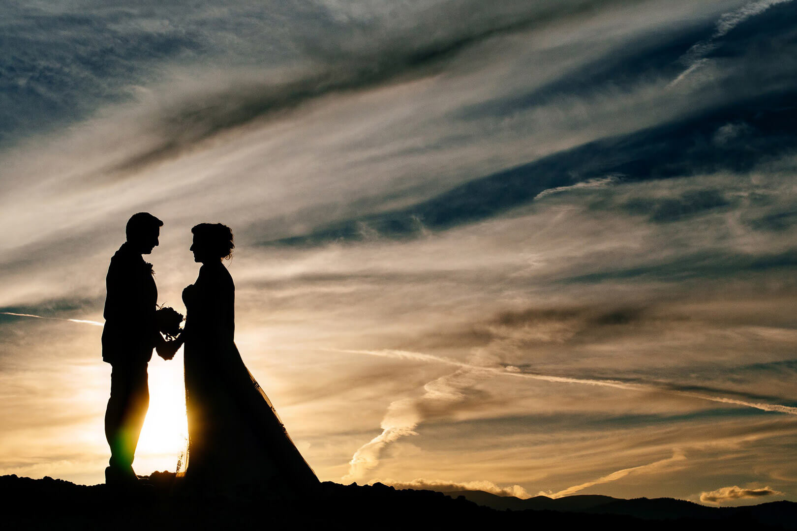 Bride and groom holding hands silhouetted against the setting sun in Meteora, Greece.