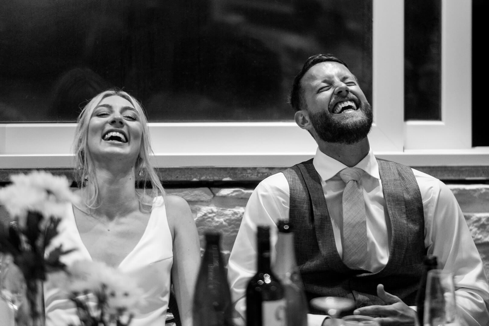 Heartfelt laughter as the couple listens to a speech, capturing a joyous and intimate moment