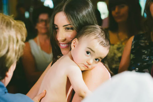 A mother's love and pride radiate as she holds her baby close at a christening ceremony in Athens, Greece.