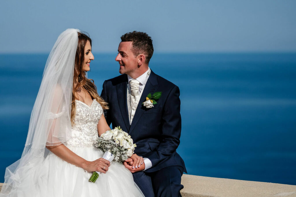 A couple popse for a portrait after their wedding ceremony in Syros, the blue of the Aegean sea in the background.